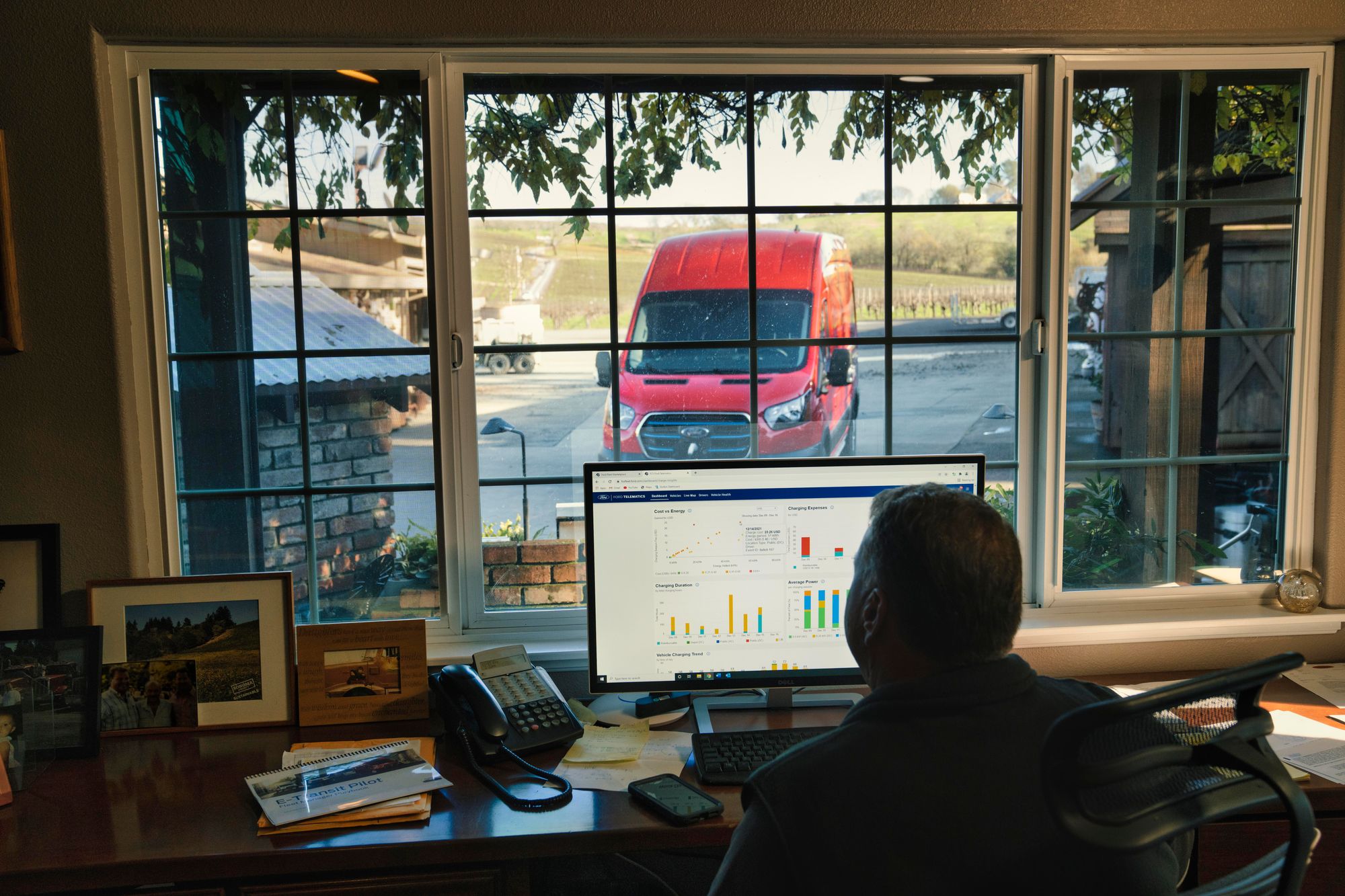 A red Ford e-transit looms in the background as a fleet manager tends to his data