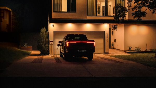 A photo of an F-150® Lightning® truck parked in a driveway plugged into a charging station during the early morning hours