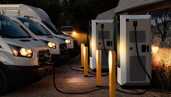 Three Ford E-Transit vans are plugged into depot chargers to charge overnight.