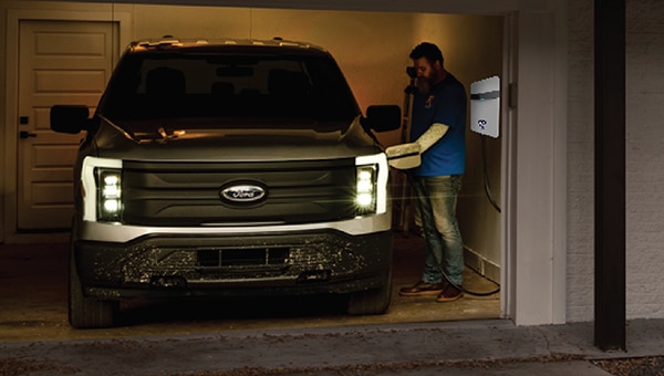 Homme qui branche un camion Ford Lightning à une borne de recharge à domicile, dans un garage.