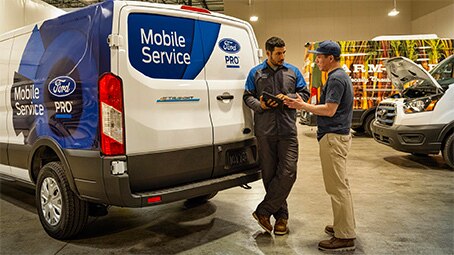 A Ford Pro Mobile Technician talking to a customer inside a warehouse. In the background is a Ford Pro Mobile Service Transit van.