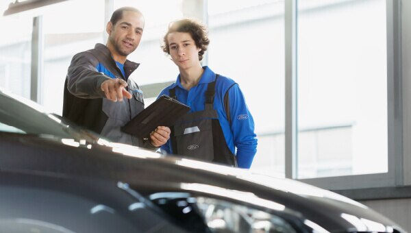 Two service technicians. One holding a tablet and pointing at a vehicle.