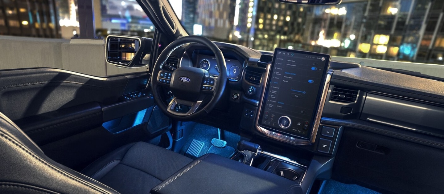 The interior of a 2024 Ford F-150 Lightning pickup truck at night, with colorful LED illumination in the footwells