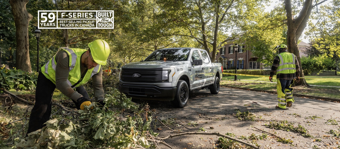 An F-150 Lightning in the background of workers cutting trees