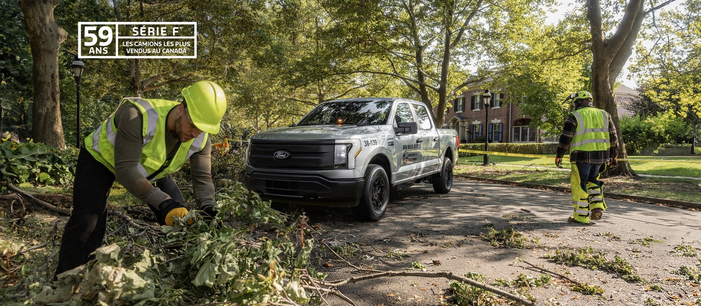 An F-150 Lightning in the background of workers cutting trees