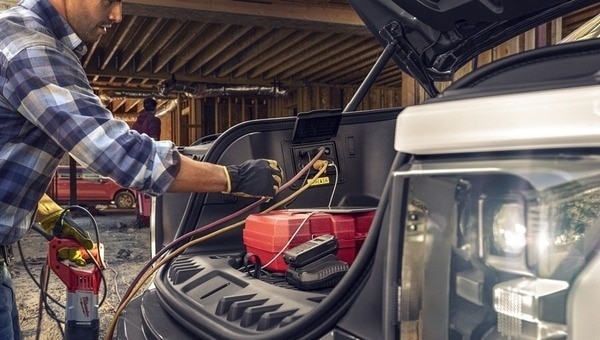 A 2023 Ford F one Fifty Pro with front trunk open and packed with gear parked at a job site