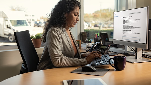 Woman working at a desk with a computer monitor using Ford AI.