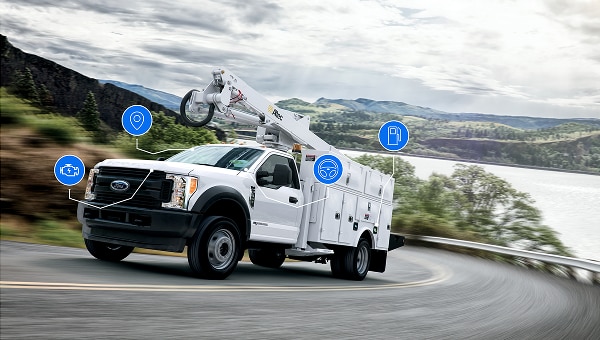 Image of a white Ford truck with utility arm driving on a curved road.