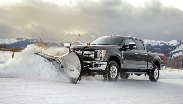 Black plow truck moving a pile of snow on the highway.