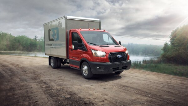 Box truck with upfitter chassis driving along a dirt road.