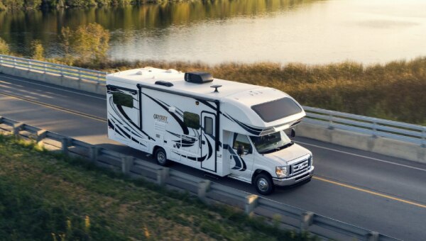 White motor home driving along a forested road.