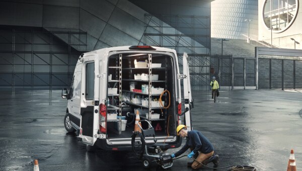 Construction worker charging a tool behind a cargo van.