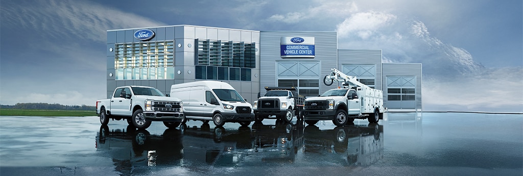 Cinco vehículos comerciales Ford, incluyendo camionetas pickups, vans y camiones de servicio, estacionados frente a un edificio del Ford Commercial Vehicle Center.