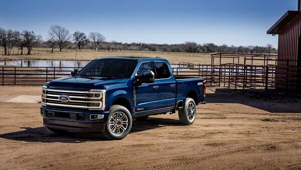 Camioneta Ford Super Duty azul estacionada en un camino de tierra, con un estanque y vallas al fondo.