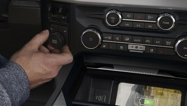 Interior de Ford Super Duty F-250 con mano ajustando el dial de modo de manejo, controles de consola y carga inalámbrica