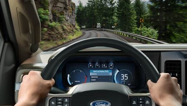 Vista desde el puesto del conductor de un Ford Super Duty, mostrando el volante, el cuadro de instrumentos digital y la proyección de velocidad en el parabrisas (Head-Up Display) mientras conduce por una carretera boscosa.
