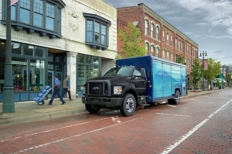 Un camion Ford negro estacionado en una calle, la caja del camión es azul y se ve a un señor transportando garrafones.