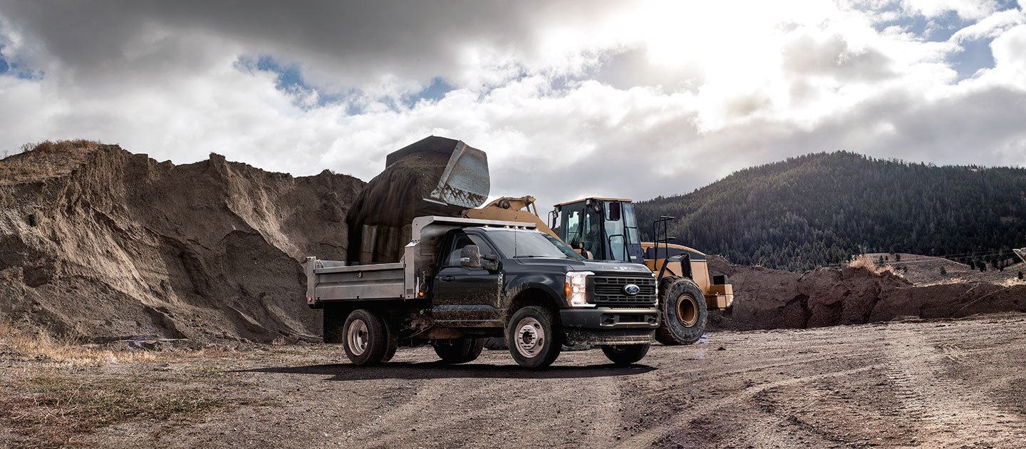 Ford Super Duty Chasis negra con caja de volteo siendo cargada con tierra por una pala cargadora en una obra.