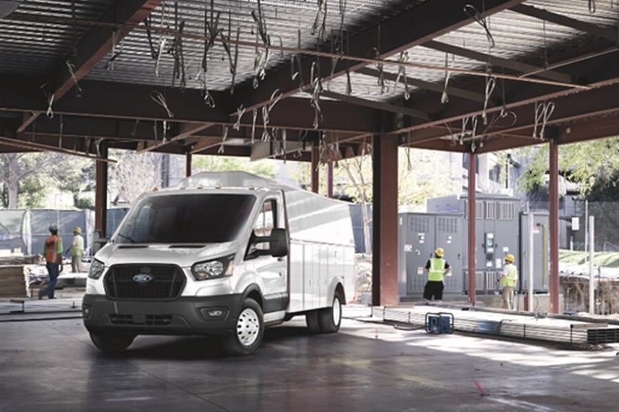 Ford Transit Chasis blanca con carrocería de servicio estacionada bajo una estructura metálica en construcción, con trabajadores.