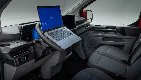 Interior de Ford Transit Custom 2026 con volante plegado para usar como mesa de trabajo con una computadora portátil.