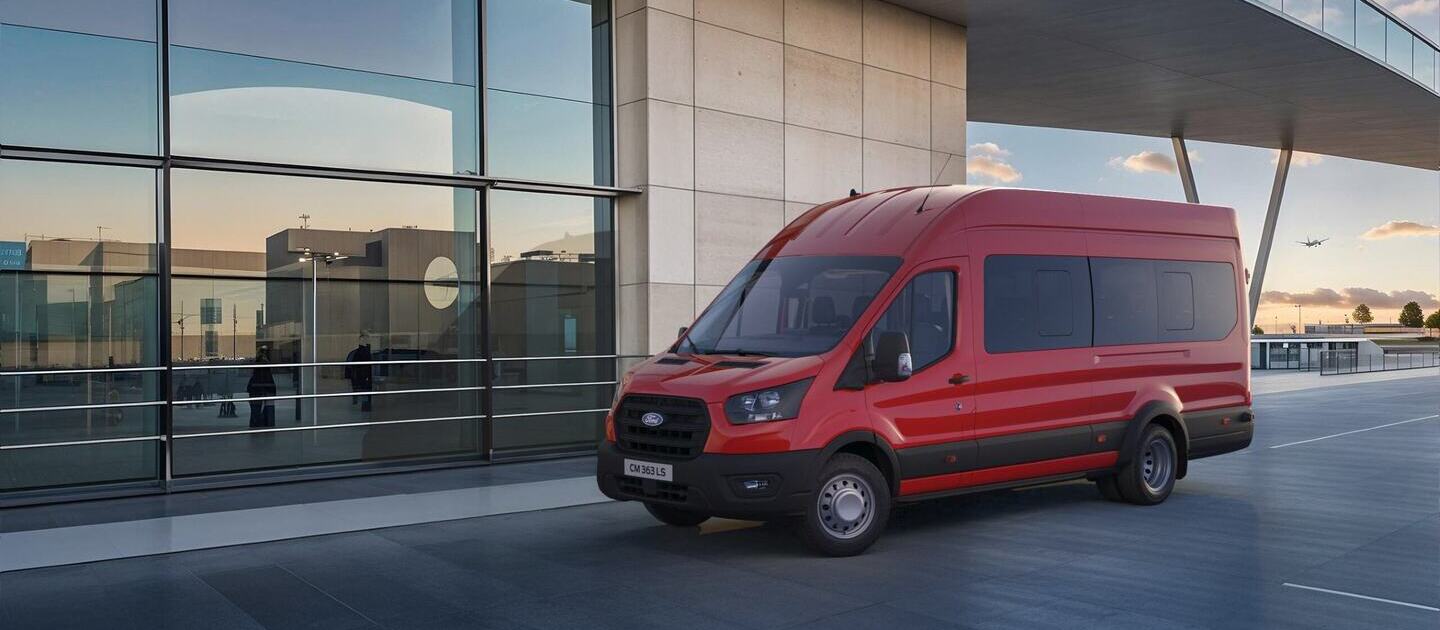 Transit de pasajeros roja estacionada frente a un edificio moderno con grandes ventanales.