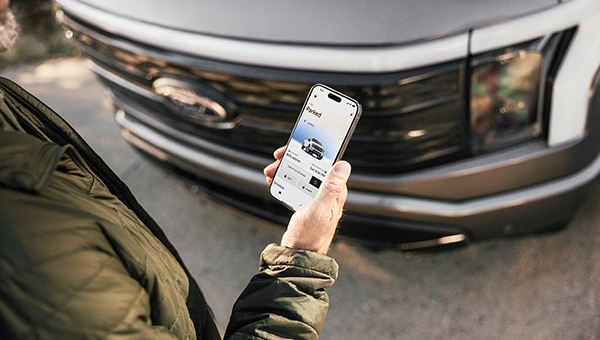 Manos sosteniendo un smartphone con la aplicación Ford app mostrando el estado de una Transit Van.