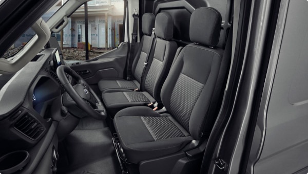Interior de Ford Transit Van con asientos de tela y vista a obra en construcción.