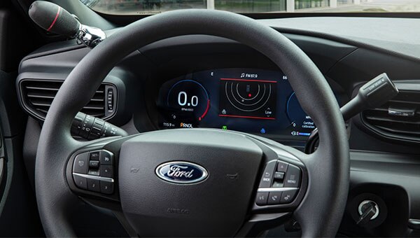 Vista frontal del interior de un Ford Police Interceptor, que muestra el volante, el tablero de instrumentos y la consola central equipada con controles  especializados para el servicio policial.
