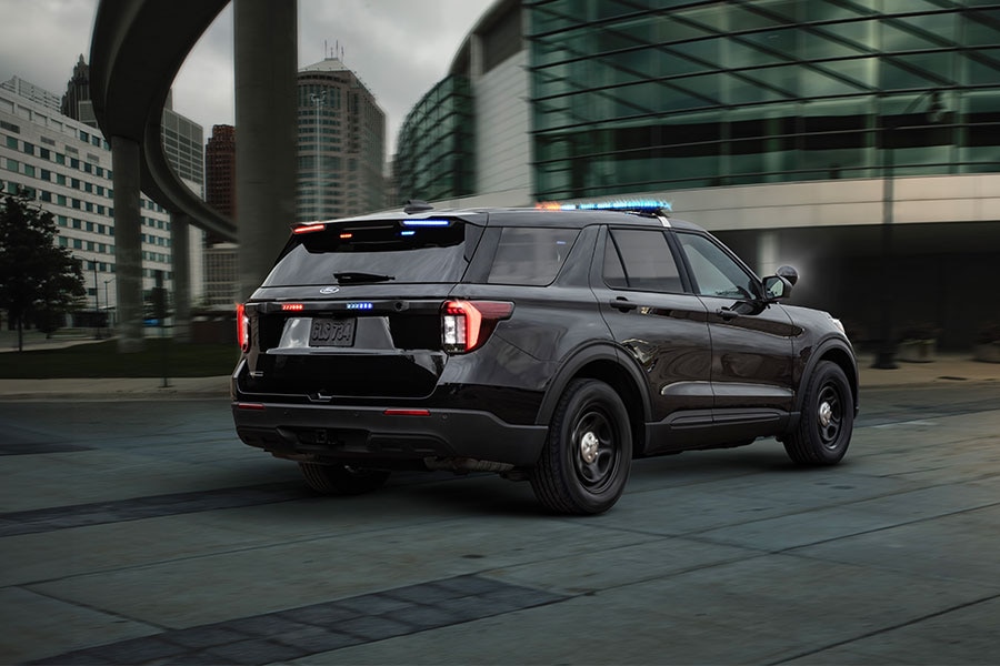 Vista trasera de Ford Police Interceptor Utility negra en una calle urbana de noche, con sus luces de emergencia rojas y azules encendidas en el techo y la parte trasera.