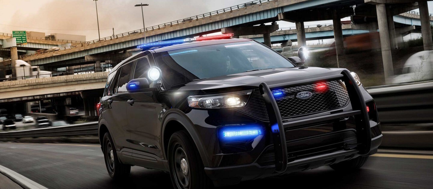Ford Police Interceptor Utility negro 2025 con luces de emergencia rojas y azules y una defensa delantera, en movimiento en una autopista