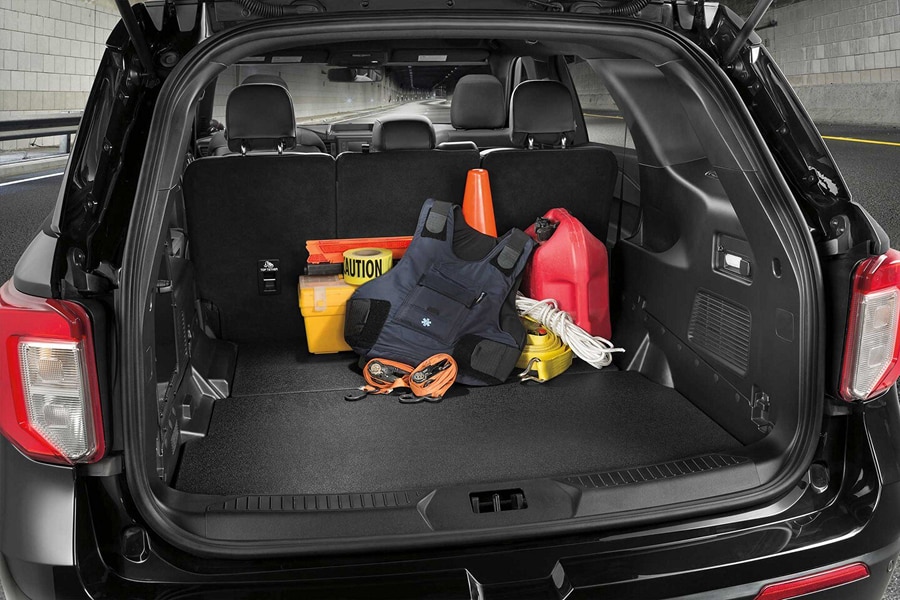 Vista del compartimento de carga trasero de Ford Police Interceptor Utility negro, con el maletero abierto. Se observa un suelo de goma resistente y varios elementos como un chaleco táctico, conos de tráfico, un bidón de gasolina rojo y cuerdas.