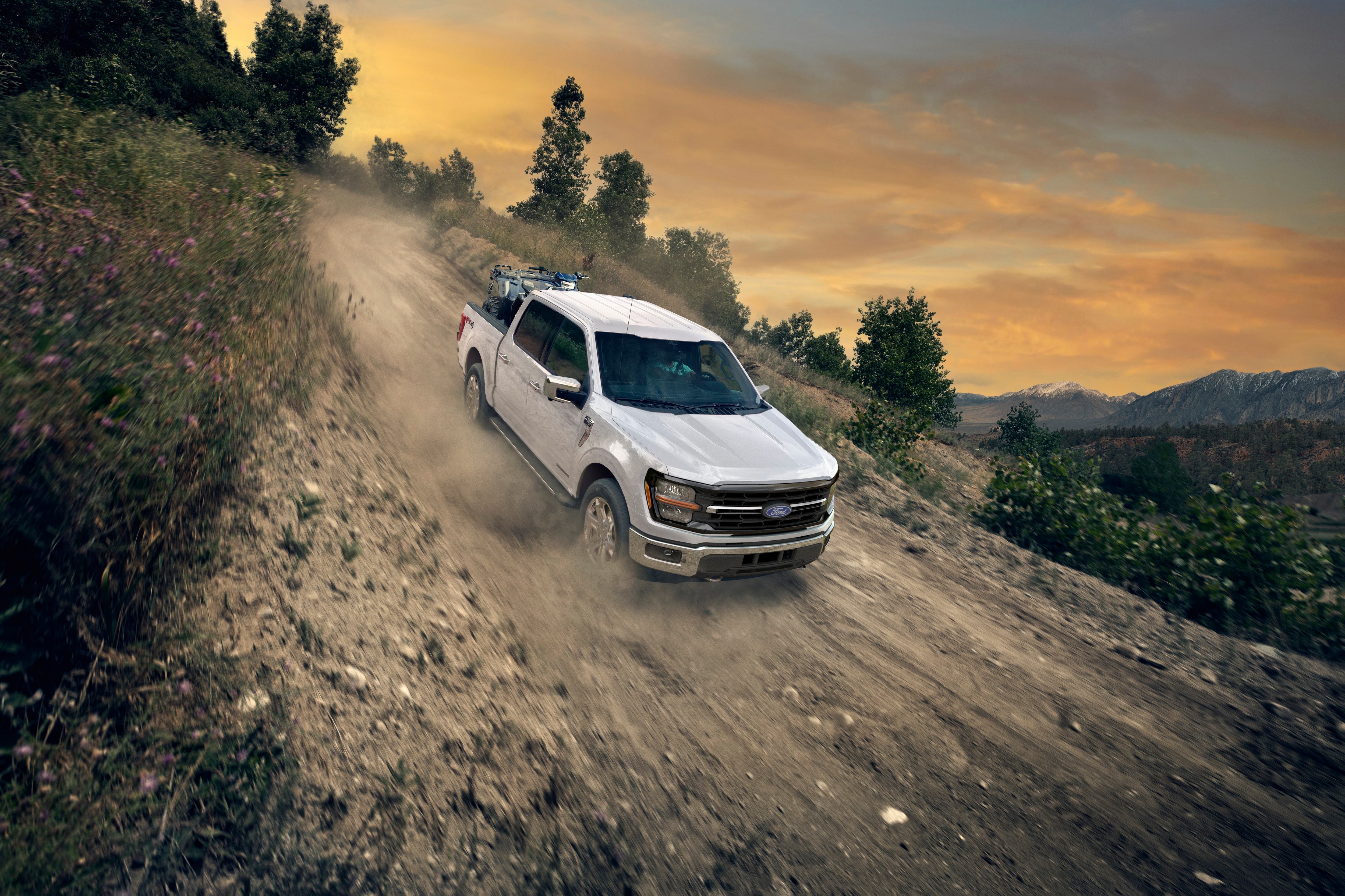F-150 blanca subiendo por camino de tierra levantando polvo, con paisaje montañoso.