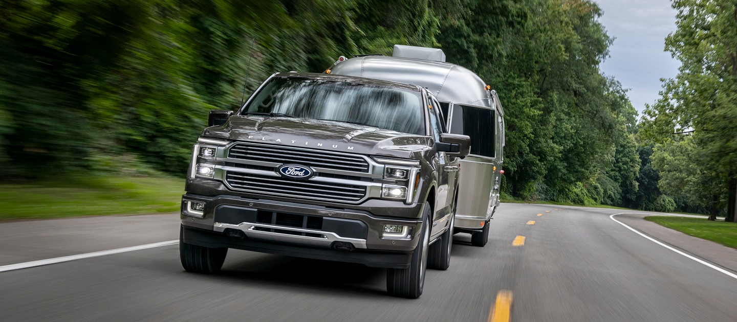 Ford Lobo Platinum gris arrastrando un remolque en una carretera boscosa y sinuosa.