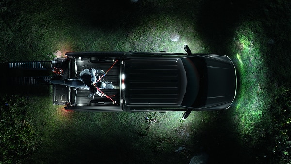 Vista aérea nocturna de Ford Lobo 2026 con todas sus luces exteriores encendidas, incluyendo la iluminación de la batea, proyectando luz alrededor del vehículo en un entorno natural.