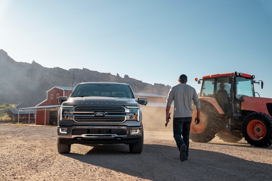 Una Ford Lobo 2026 estacionada en un camino de tierra, con un hombre caminando hacia un tractor y montañas al fondo, sugiriendo un entorno rural y de trabajo pesado.