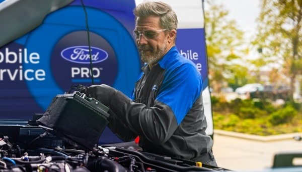 Técnico de Servicio Móvil Ford Pro realizando mantenimiento de motor en sitio.