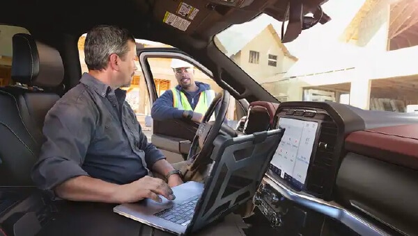 Driver side interior of truck with man on laptop talking to worker