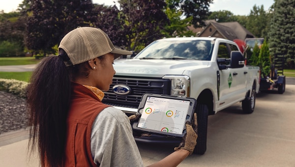 Driver using a tablet beside a white Ford Pro pickup truck in a residential neighborhood.