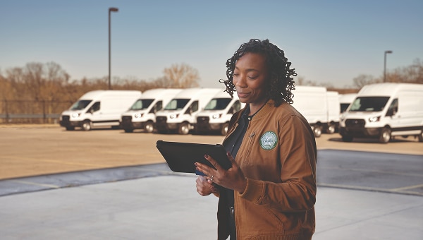 Fleet manager using a tablet while standing in front of parked Ford Pro vans.