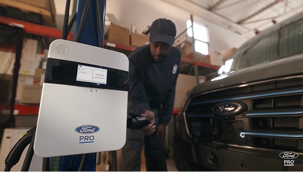 Image of a man reaching for a charging plug from a Ford Pro charger with a play icon in the bottom left corner.