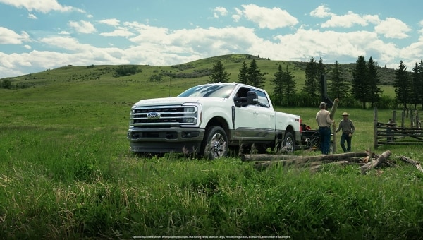 Ford Super Duty white pickup parked by rustic fence in rolling green hills.