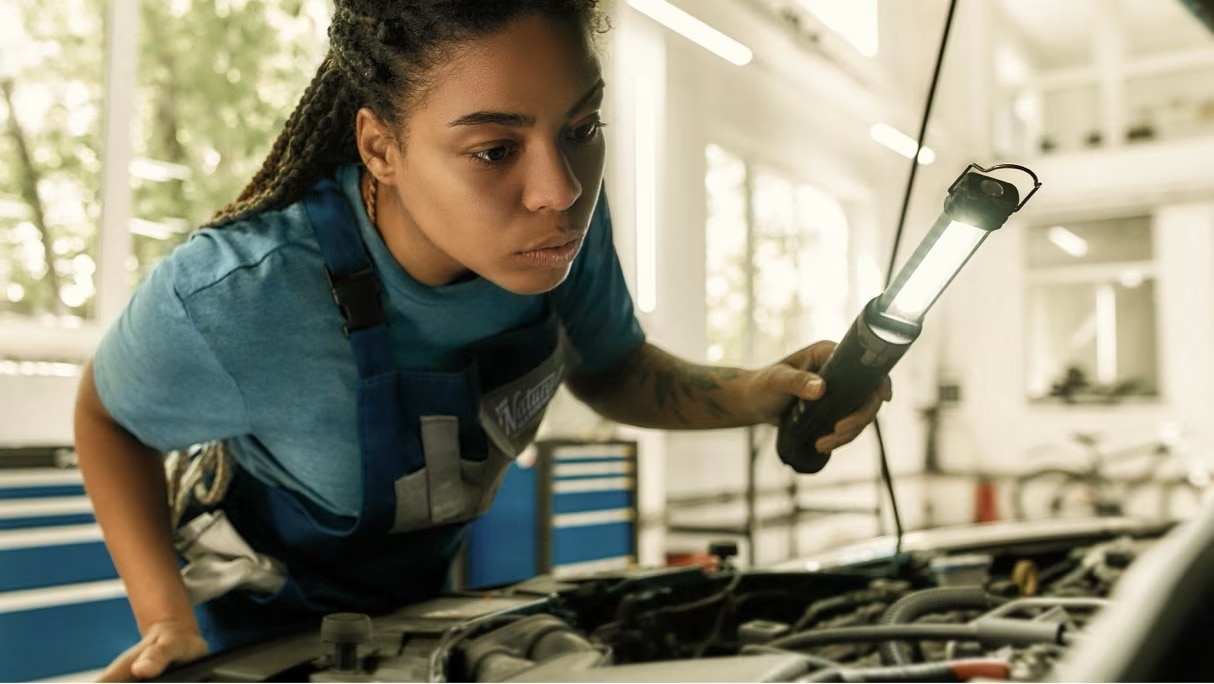 A mechanic leans over the engine of a vehicle, inspecting it.