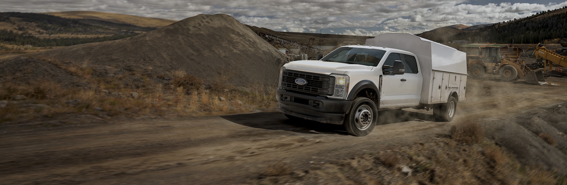 A white Super Duty Chassis Cab with a service body upfit drives on dusty road toward a job site.