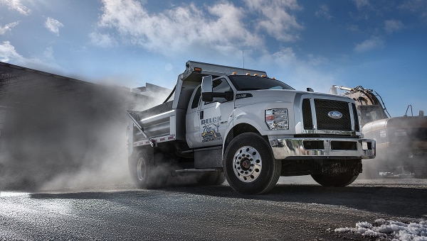 White Ford Super Duty commercial truck with a dump body upfit working on a construction site.