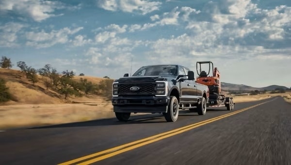 A black Super Duty pickup truck tows orange construction equipment while driving on a highway. 