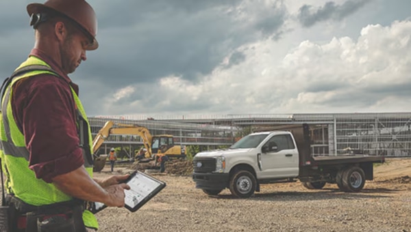 Man looking at a tablet screen on a jobsite. A Ford truck is in the background.
