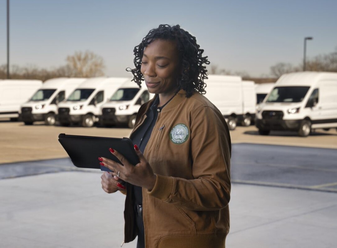 Female fleet manager stands in front of her Transit fleet vehicles looking at her tablet