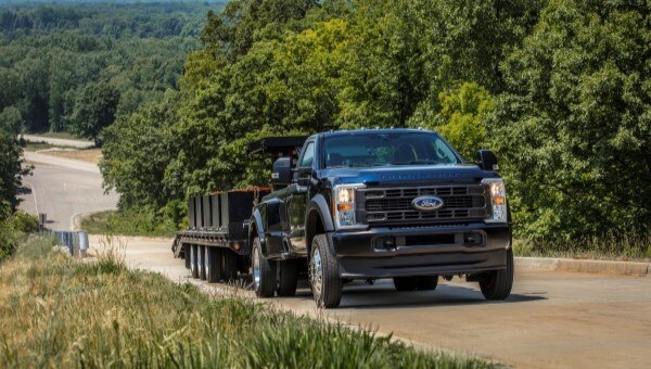 Ford Super Duty truck towing a heavy trailer uphill on a test track surrounded by trees.
