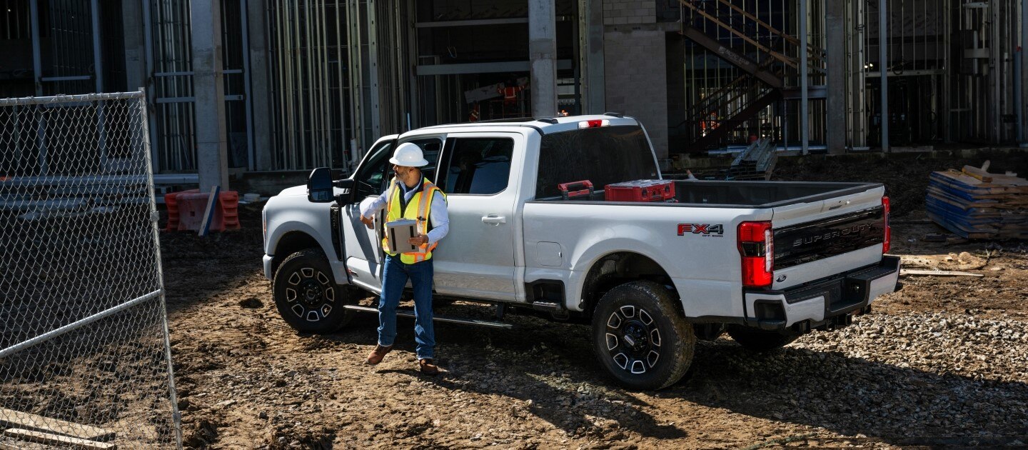 White Ford Pro pickup truck parked at a construction site, with a worker in safety gear standing beside it.
