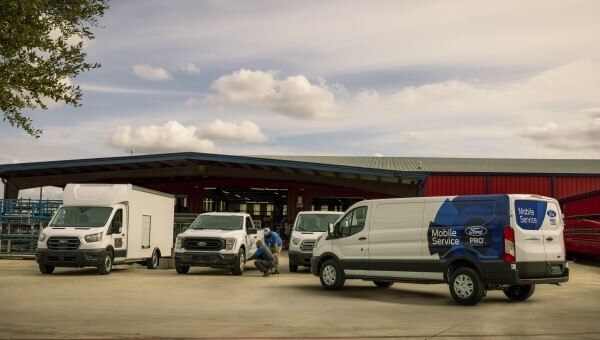 Ford Pro Mobile Service van parked outside a service center with technicians working on nearby fleet vehicles.